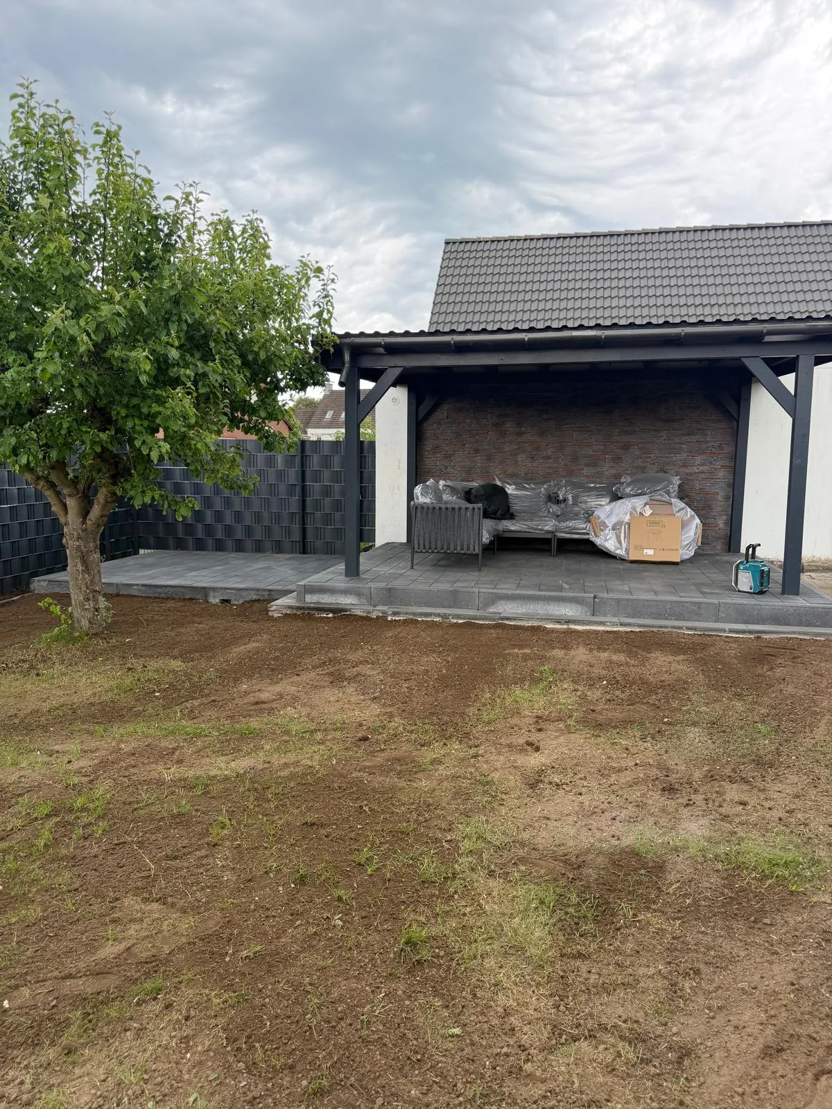 Gartenfläche mit freiliegender Erde vor einer überdachten Terrasse
